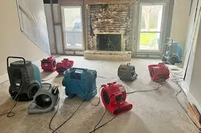 Two dehumidifiers and several air movers drying a carpeted living room after a leak