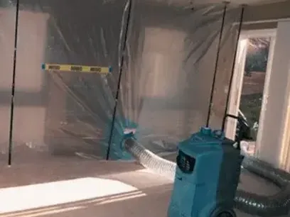Dehumidifier running inside a plastic containment area while a room dries after a leak