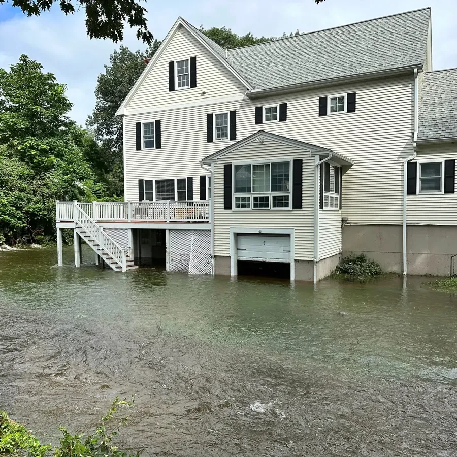 Floodwater surrounding a white two-story house and its garage door after heavy rain