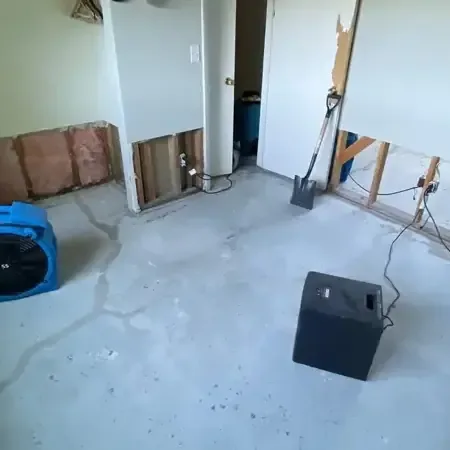 Air movers and a dehumidifier working in an emptied room where the lower drywall was cut away and the floor left bare